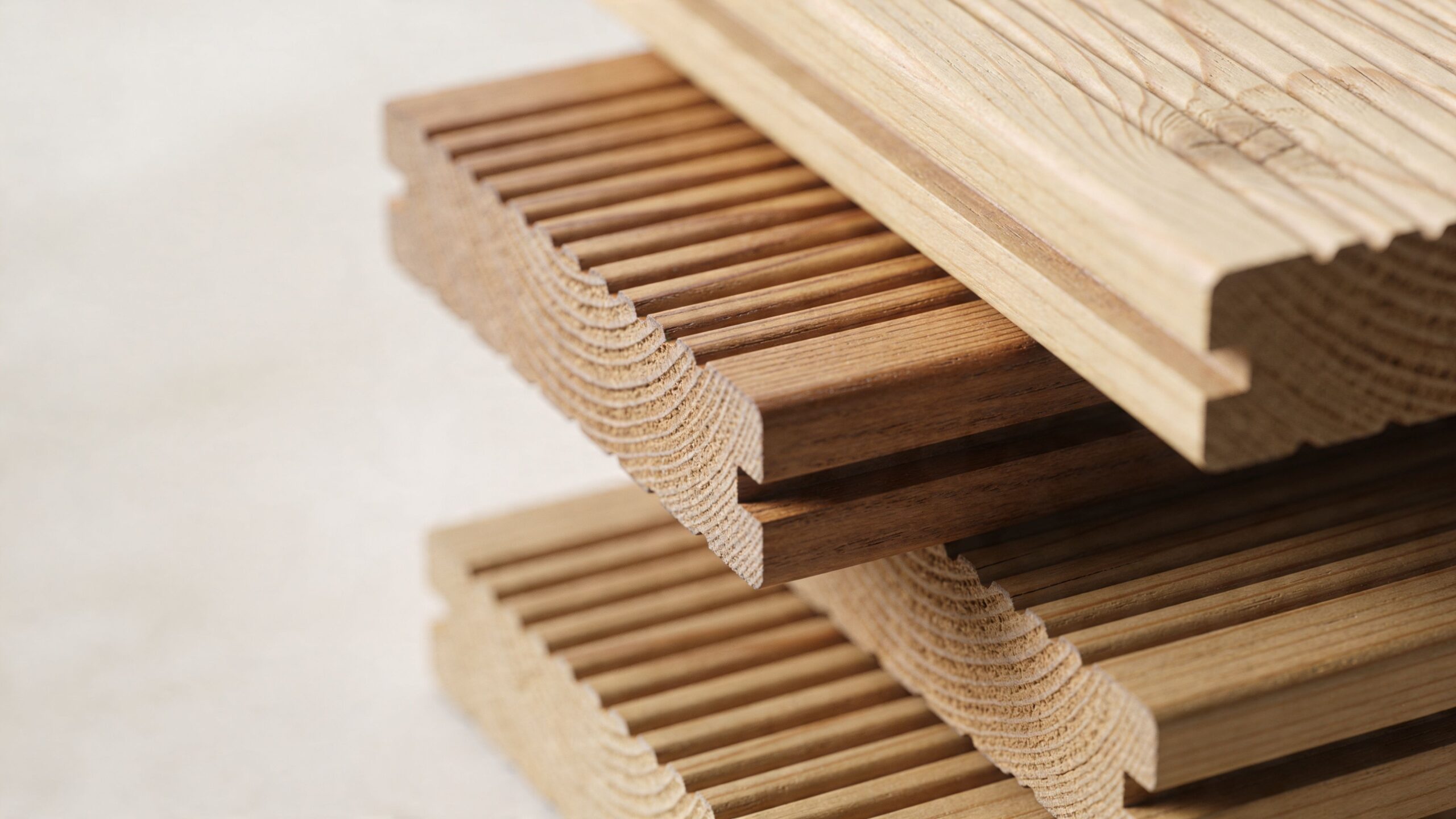 Nærbillede af stabelte træplanker til terrasser med synlige årer og riller på en lys baggrund.