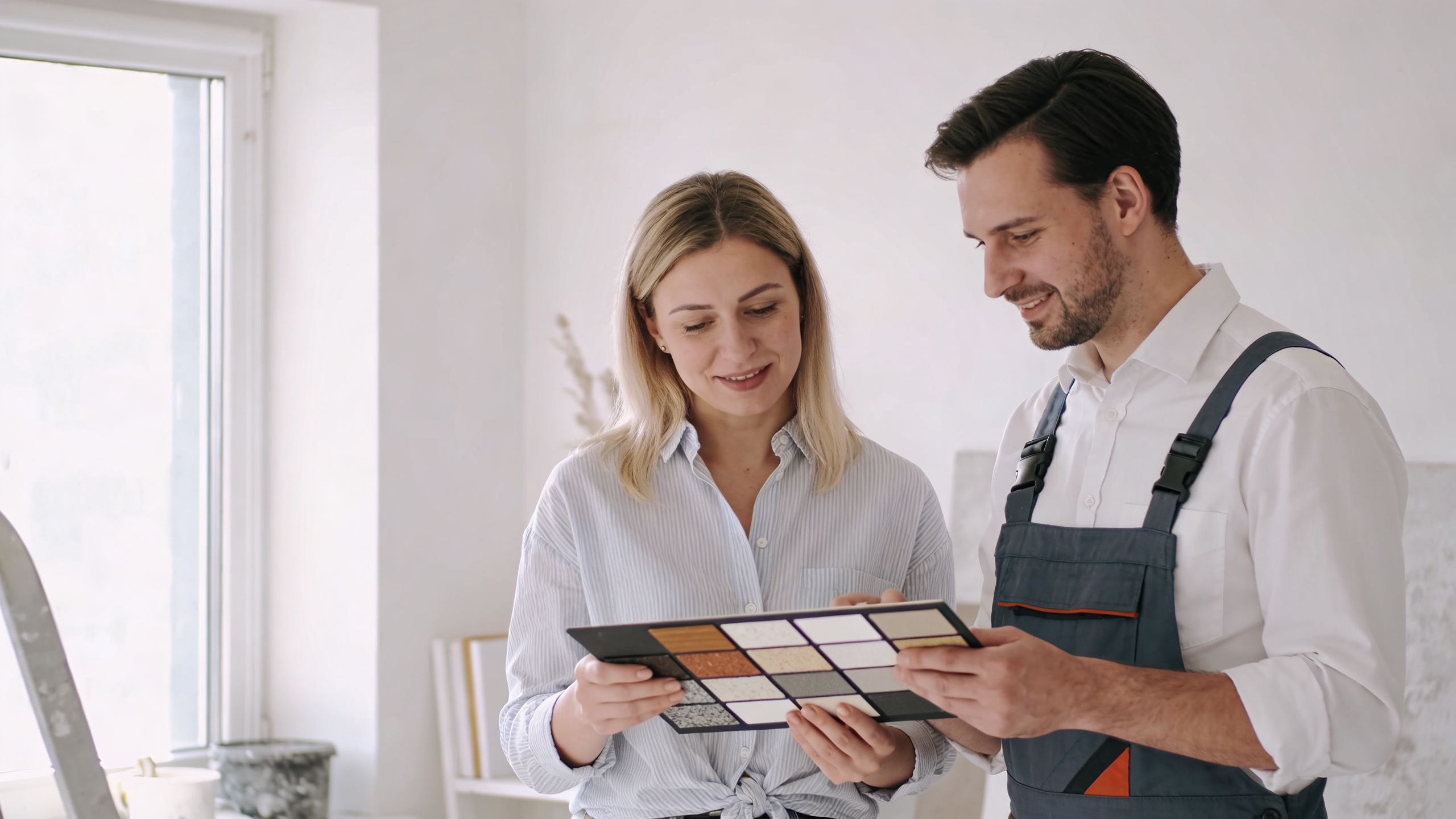 En kvindelig kunde og en mandlig håndværker kigger på materialeprøver under en renovering af en lejlighed.