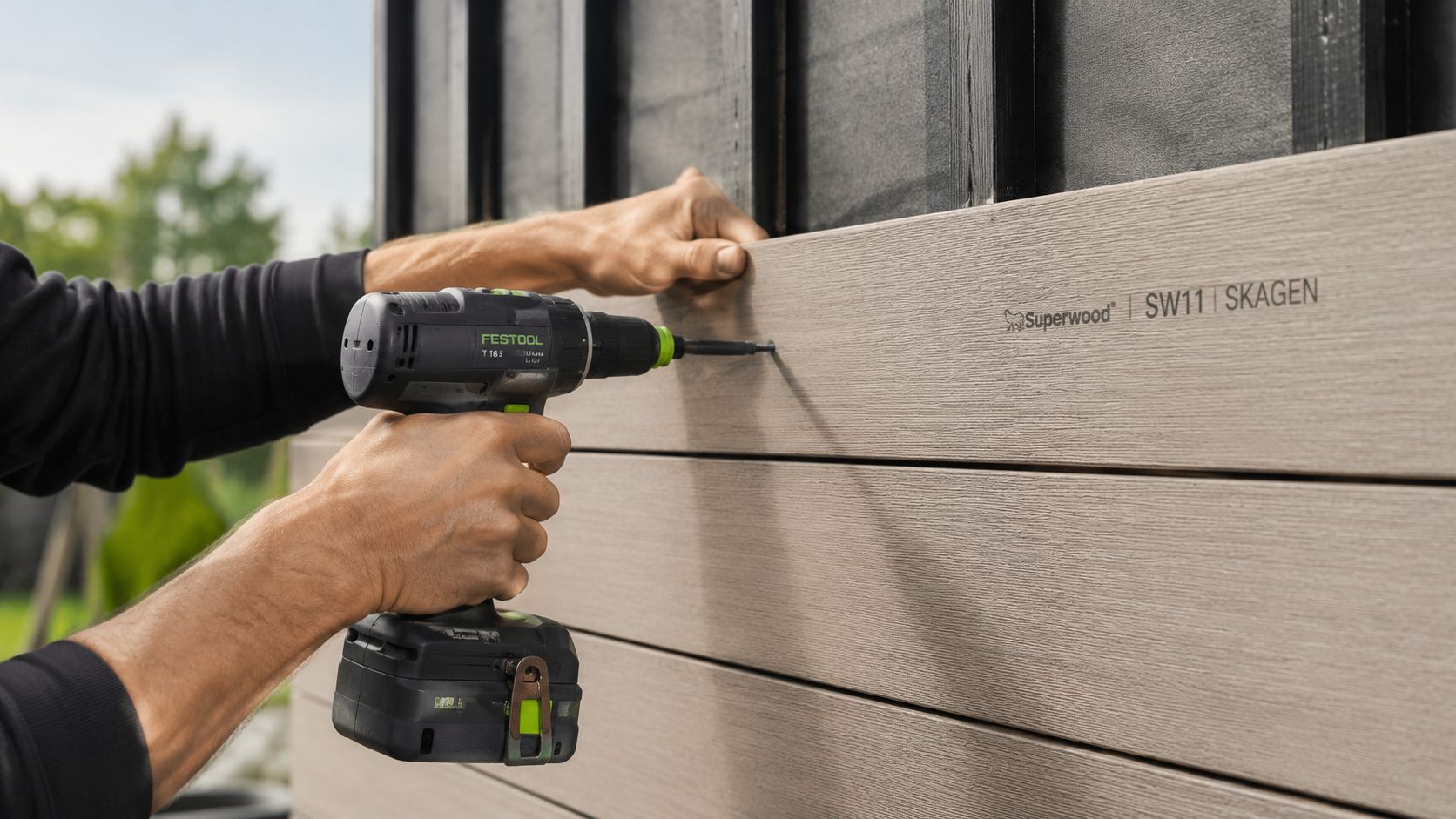 En håndværker monterer Superwood SW11 SKAGEN beklædningsbrædder på en husfacade ved hjælp af en Festool boremaskine.