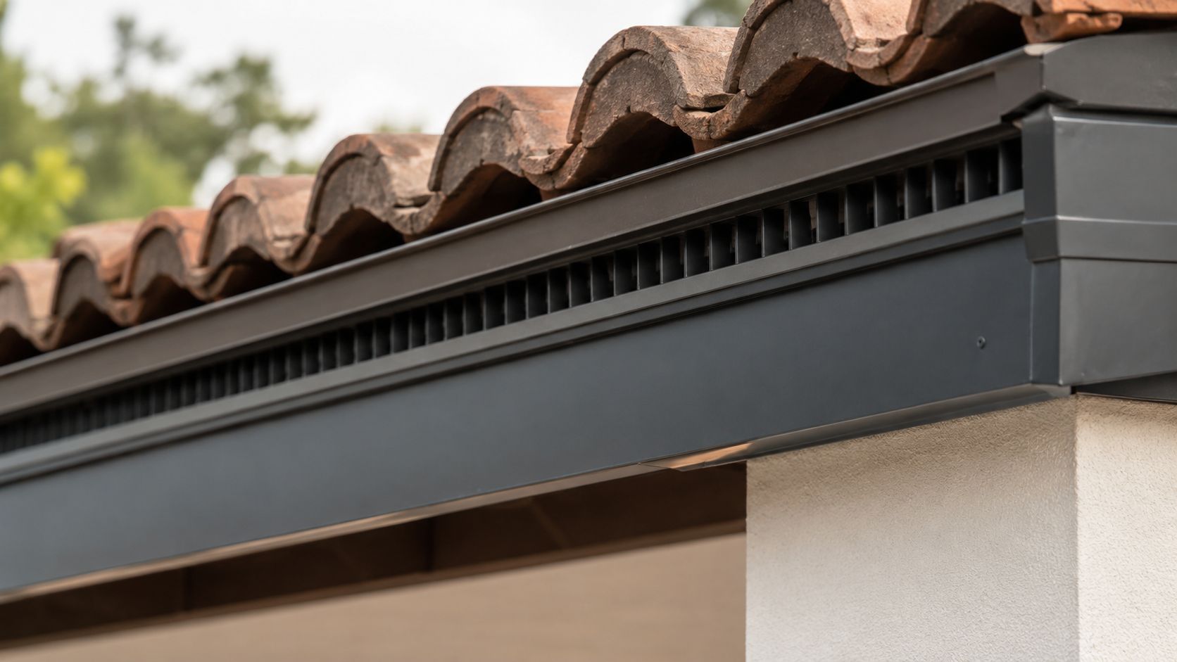 Nærbillede af en moderne tagkonstruktion med ventilationsåbninger under de traditionelle rødbrune tagsten og en hvid facade.