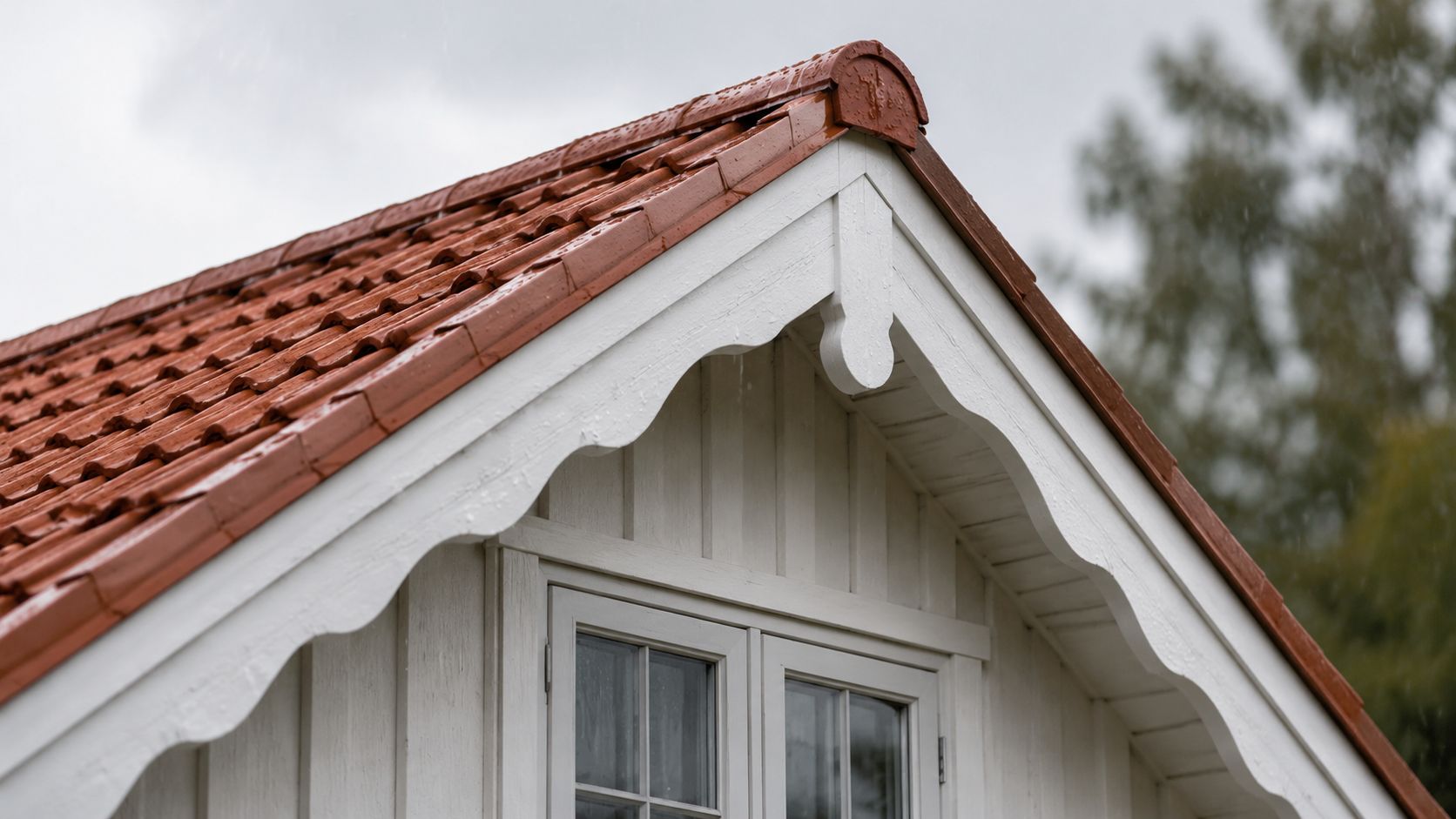 Nærbillede af et hvidmalet trægavlsudhæng med røde tagsten på et hus i regnvejr.
